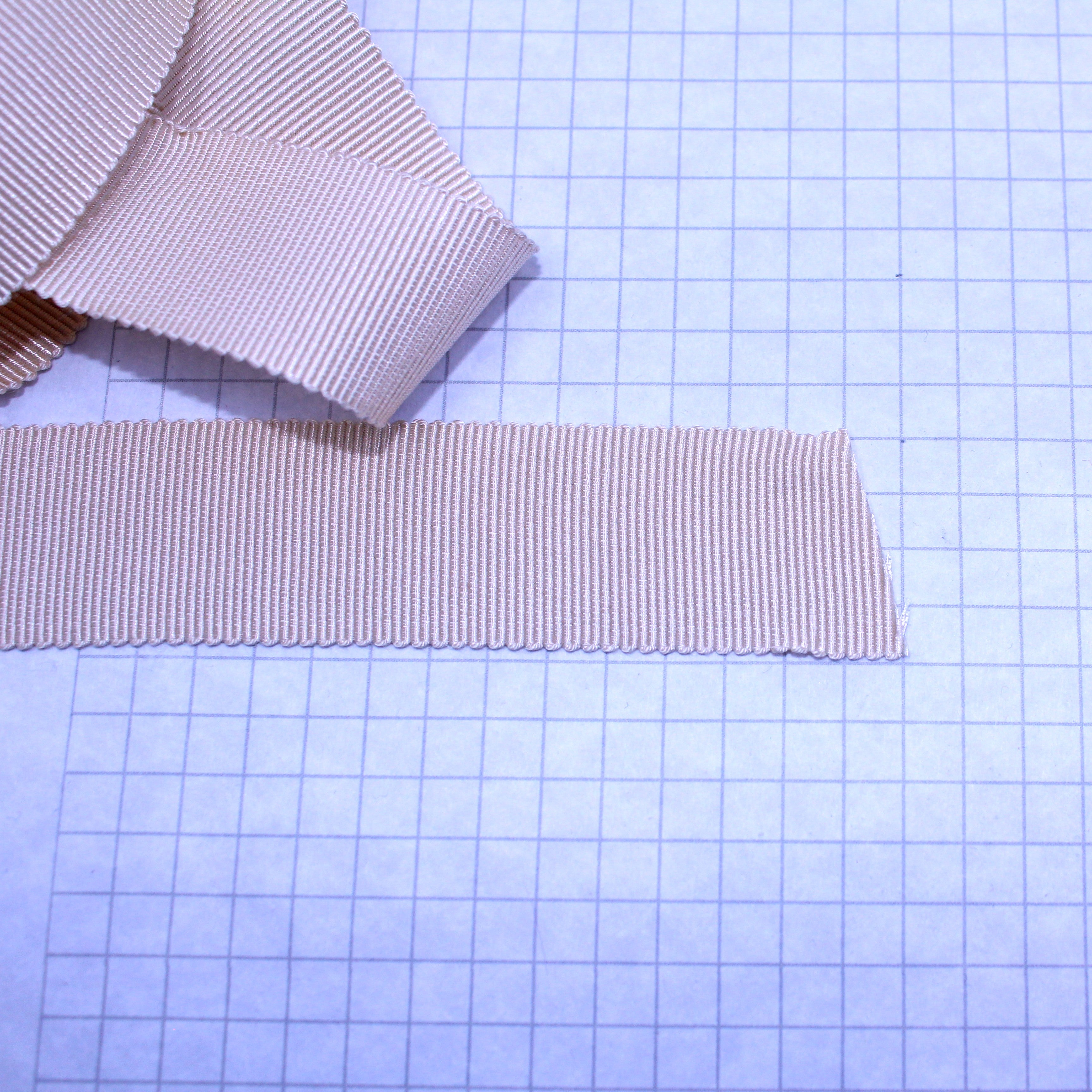 Beige petersham ribbon and a grid of 1/4" inch squares. Showing the size.