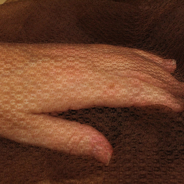 A fair skinned hand shows the detail of this dark brown soufle fabric, which would be invisible on dark skin